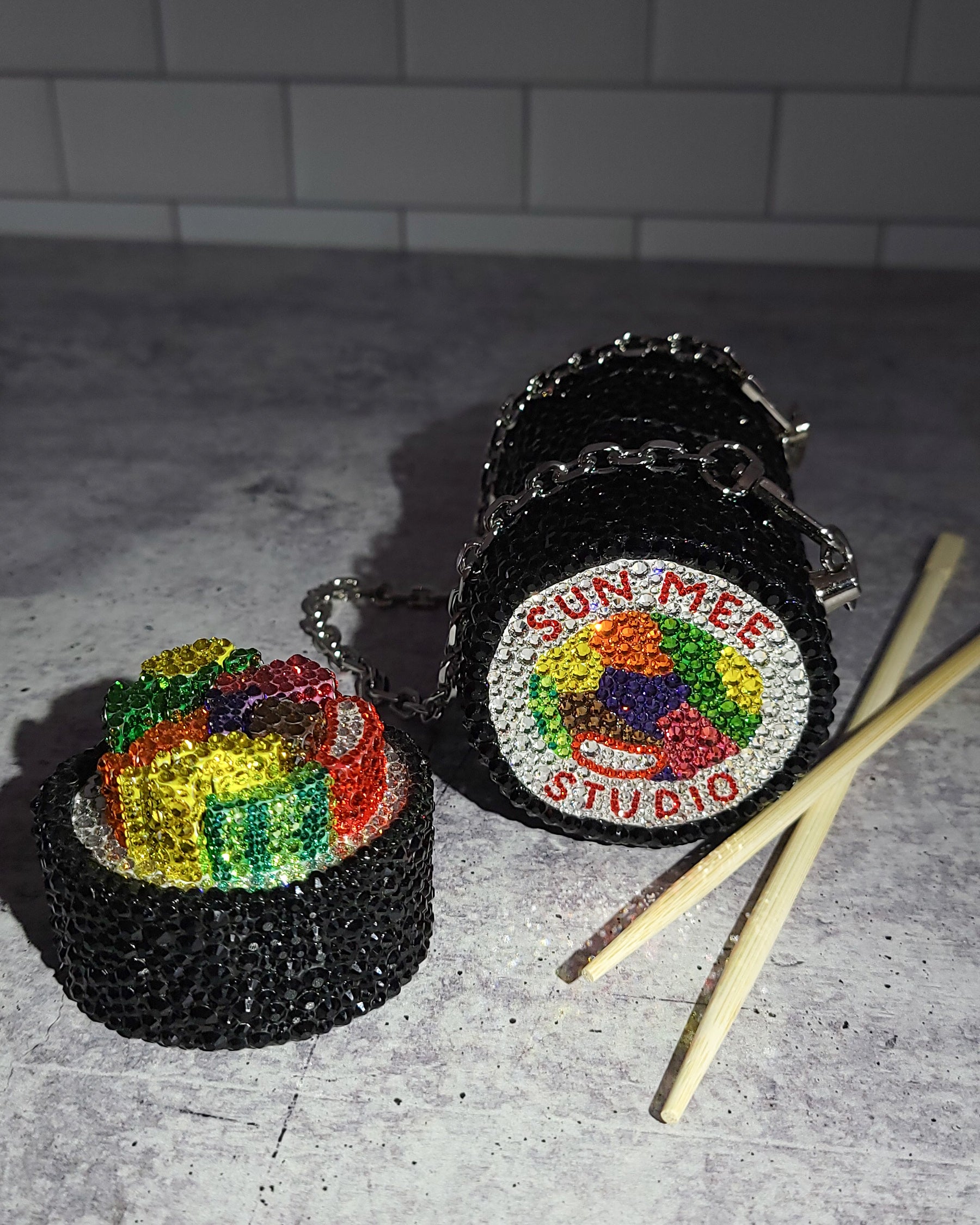 GIMBAP Purse with the top twisted off to demonstrate the screw off style, styled with a pair of chopsticks, showing the bottom of the purse, featuring a handpainted motif.